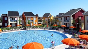 A swimming pool surrounded by colorful buildings with outdoor seating and umbrellas. - Green Village by Interhome (Lido di Jesolo)