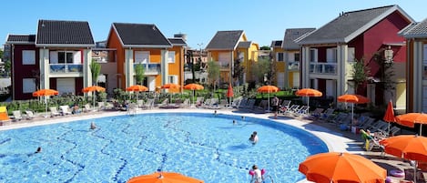A swimming pool surrounded by colorful buildings with outdoor seating and umbrellas.
