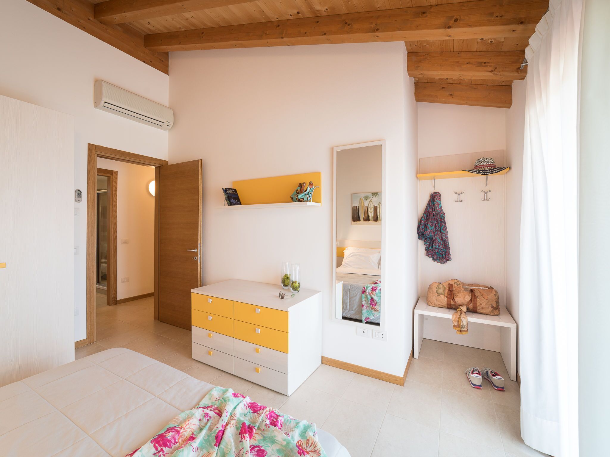A bedroom with a bed, a dresser, a wardrobe, a bedside table, a shelf with decorative items, and a hanging hat.