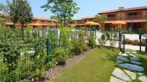 A courtyard with a pool, surrounded by a fence, and a building with balconies and orange umbrellas. - Villaggio Tamerici by Interhome (Lignano Sabbiadoro)