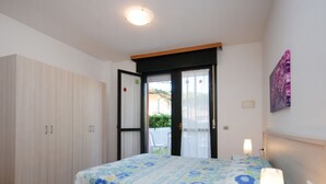 Quarto com cama, mesa de cabeceira, guarda-roupa e porta que dá para uma área externa.