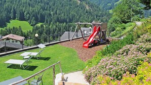 A playground with a red slide, surrounded by a grassy area and a forested hillside. - Ornella by Interhome (Santa Cristina)