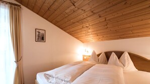 A bedroom with a wooden ceiling, a bed with white bedding, a nightstand with a lamp, and a framed picture on the wall. - Ornella by Interhome (Santa Cristina)