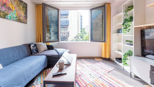 A modern living room with a sofa, a coffee table, a TV, and a large window with curtains.