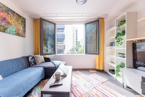A modern living room with a sofa, a coffee table, a TV, and a large window with curtains.
