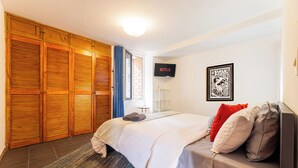 A bedroom with a bed, a TV, a wardrobe, and a framed picture on the wall.