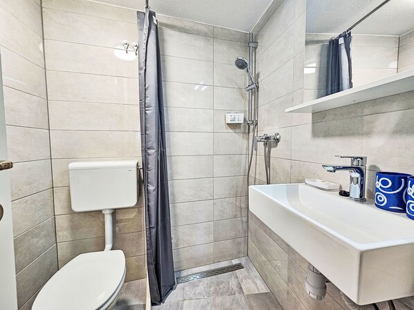 A modern bathroom with a toilet, shower, and sink.