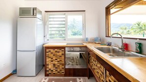 Une cuisine compacte dotée d’un réfrigérateur intégré, d’une fenêtre avec stores, d’un évier et d’un pare-éclaboussures en bois.