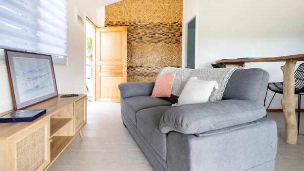 Un salon moderne avec un canapé gris, un buffet en bois et un mur à texture.
