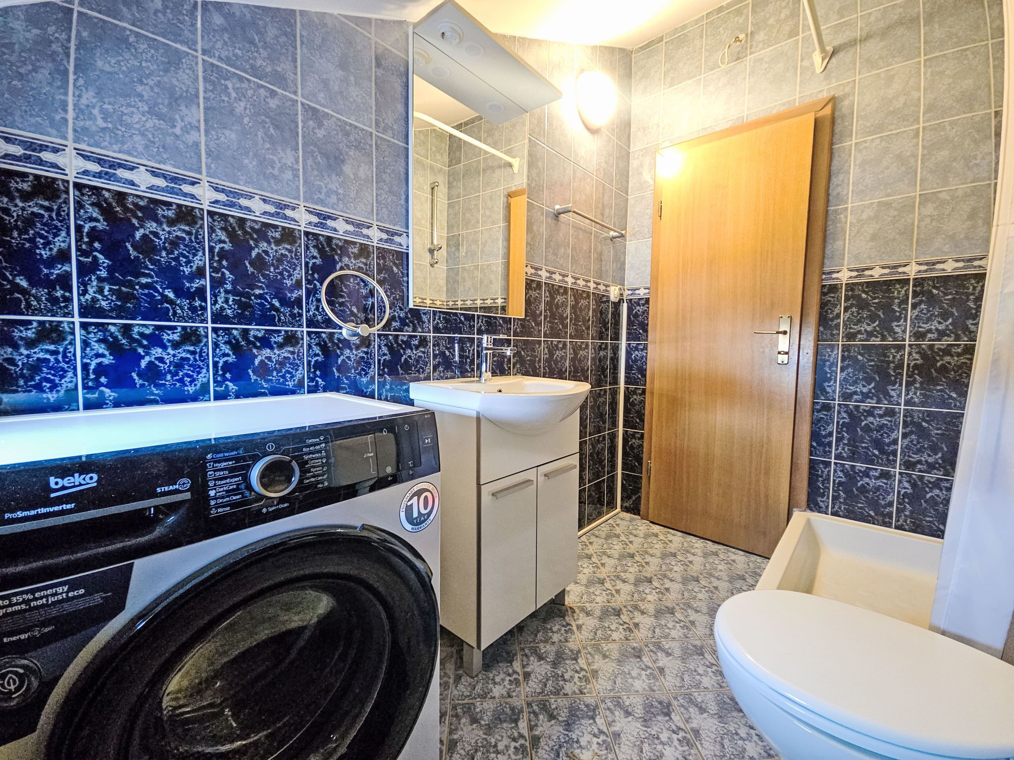 A compact bathroom with a washing machine, a sink, and a toilet.