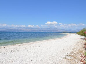 A beach with clear water, a pebble shore, and mountains in the background.
