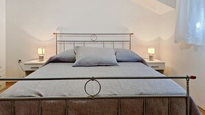 A bed with a metal frame and wooden headboard, two bedside tables with lamps, and a window with a curtain. - Vacation home Gorana by Interhome (Brač/Splitska)