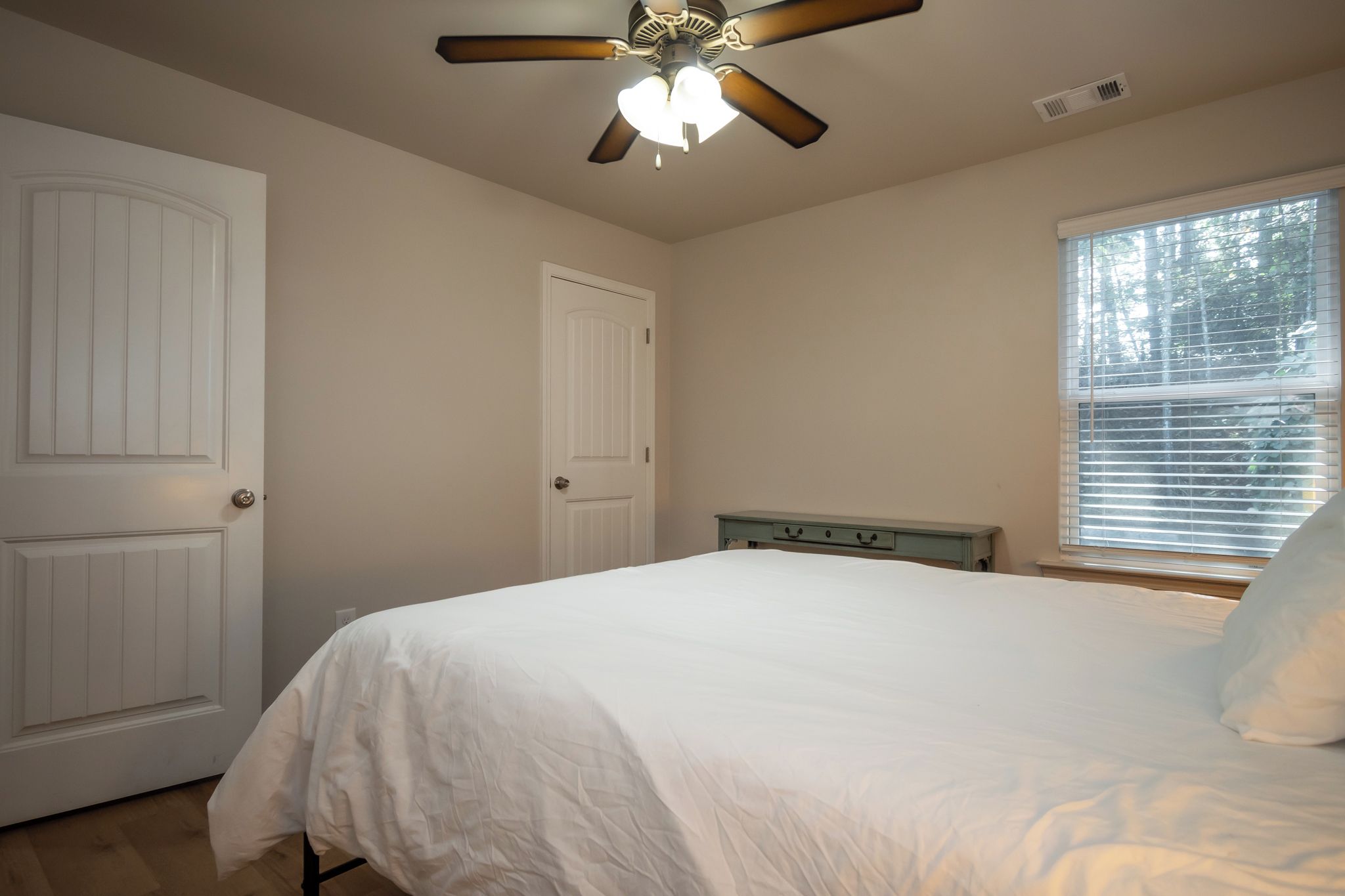 A bedroom with a bed, a ceiling fan, a window with blinds, and two doors.