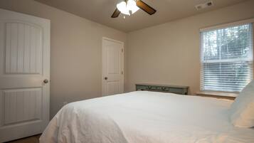 A bedroom with a bed, a ceiling fan, a window with blinds, and two doors.
