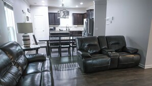 A modern living room with a leather sofa, a dining area with a table and chairs, and a kitchen with dark cabinets and a refrigerator. - Pet-friendly home minutes from Downtown/UGA Campus (Athens)