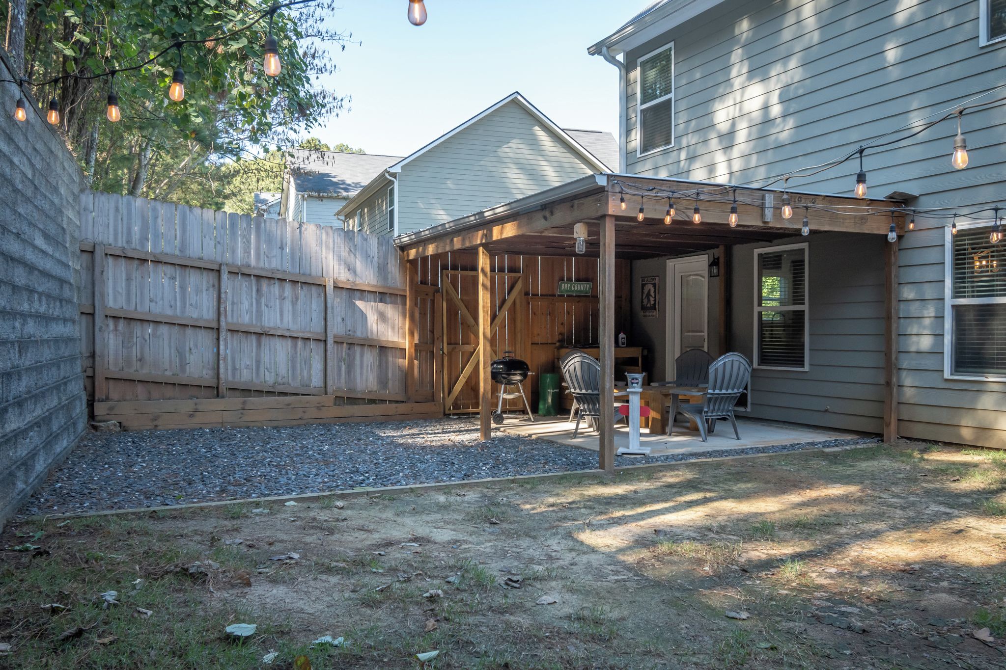 A backyard with a covered patio area, a barbecue grill, and outdoor seating.