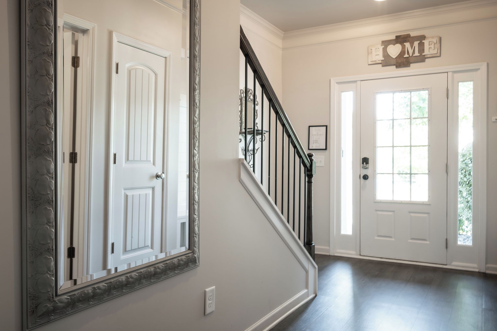 Um corredor com escada, uma porta com a placa 'HOME' e um espelho com moldura decorativa.
