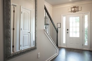 Un couloir avec un escalier, une porte portant l’inscription « MAISON » et un miroir avec un cadre décoratif.