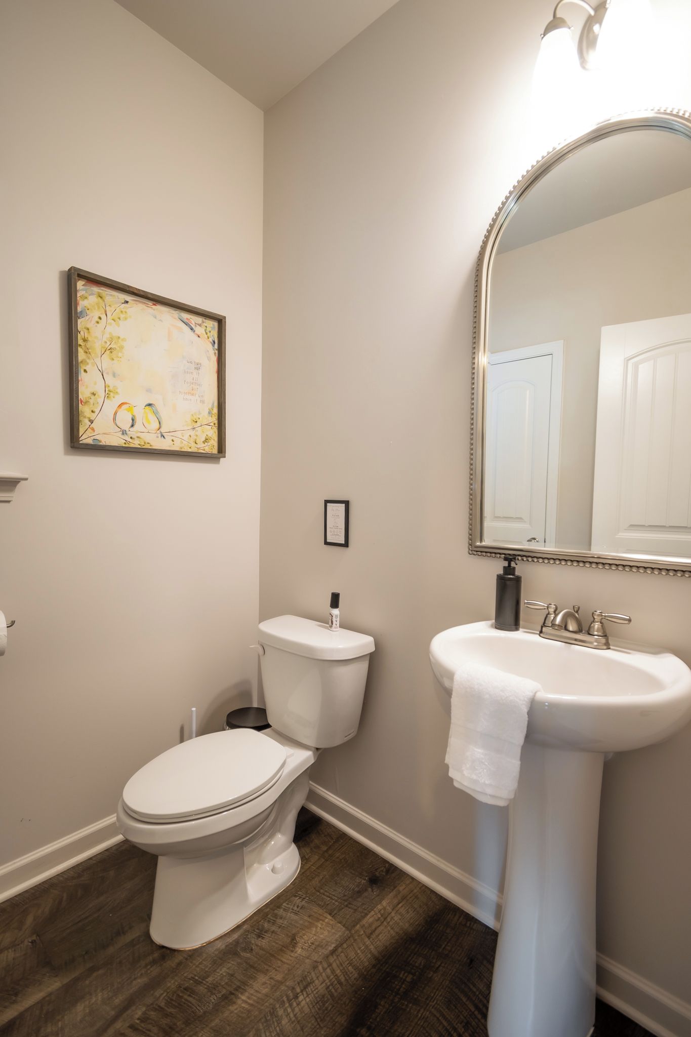 A bathroom with a toilet, sink, and a framed artwork on the wall.