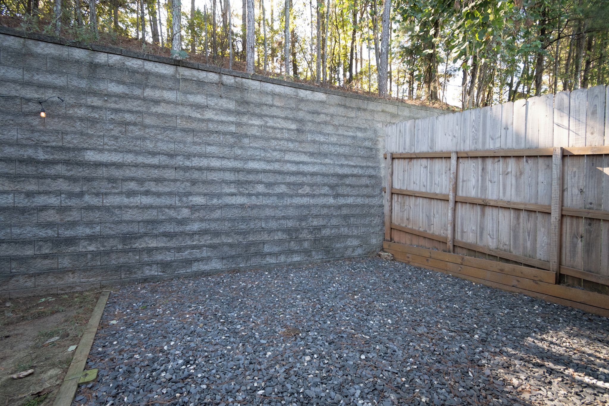 Eine Betonmauer mit Holzzaun, Kiesgrund und einer Holzterrasse.