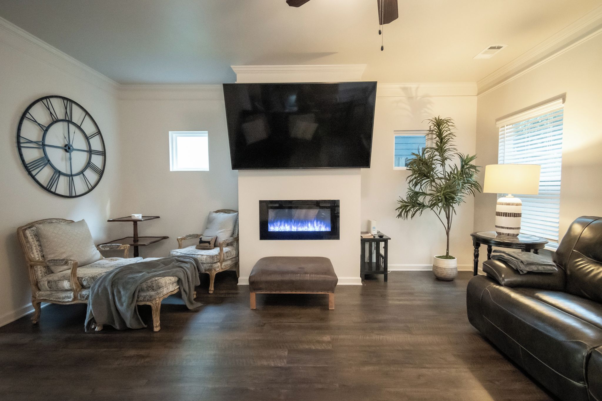 A living room with a fireplace, a large flat-screen TV, a clock, and a potted plant.