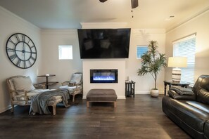 Una sala de estar con chimenea, un televisor de pantalla plana grande, un reloj y una planta en maceta.