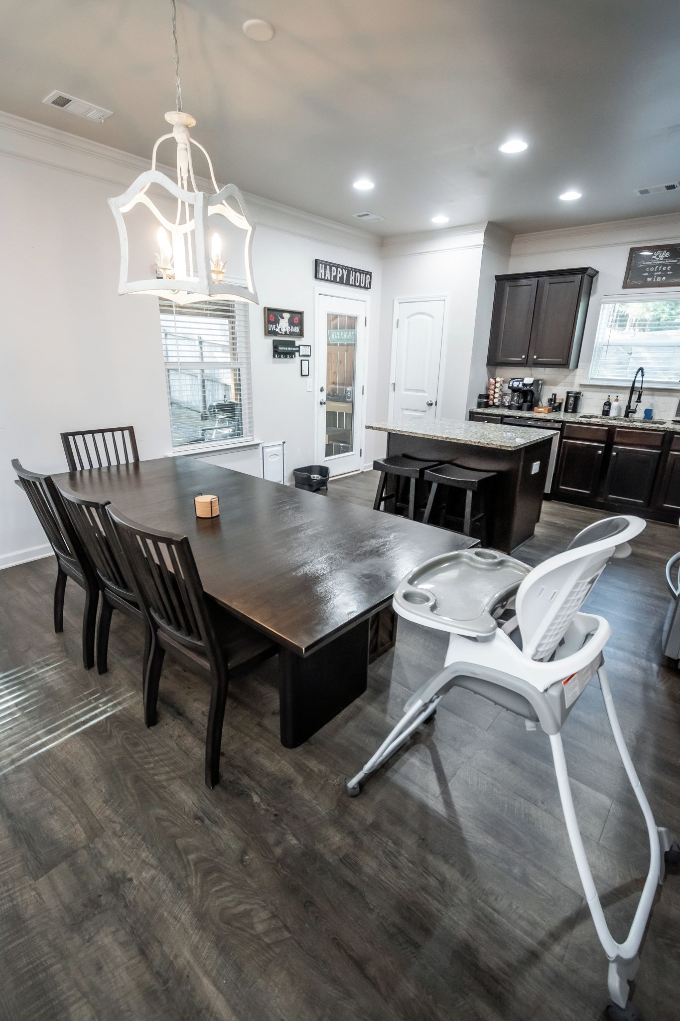 A modern kitchen with dark wood cabinetry, a central island, and a dining area with a dark wood table and chairs.
