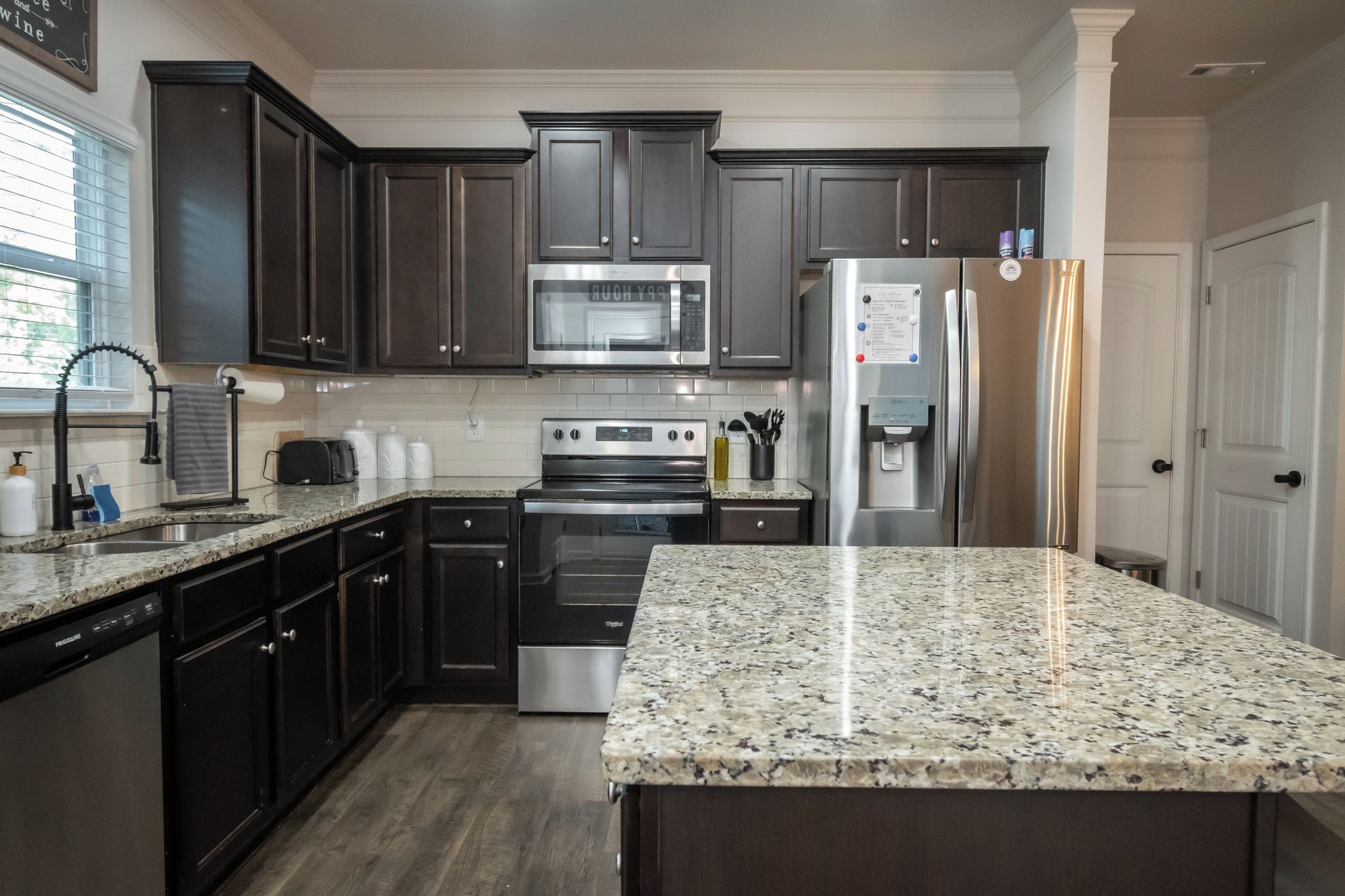 A kitchen with dark wood cabinets, stainless steel appliances, granite countertops, and a built-in oven.
