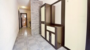 A hallway with a tiled floor, a stone accent wall, and a wooden cabinet with a mirror and hooks. - Apartment Josip by Interhome (Vodice)