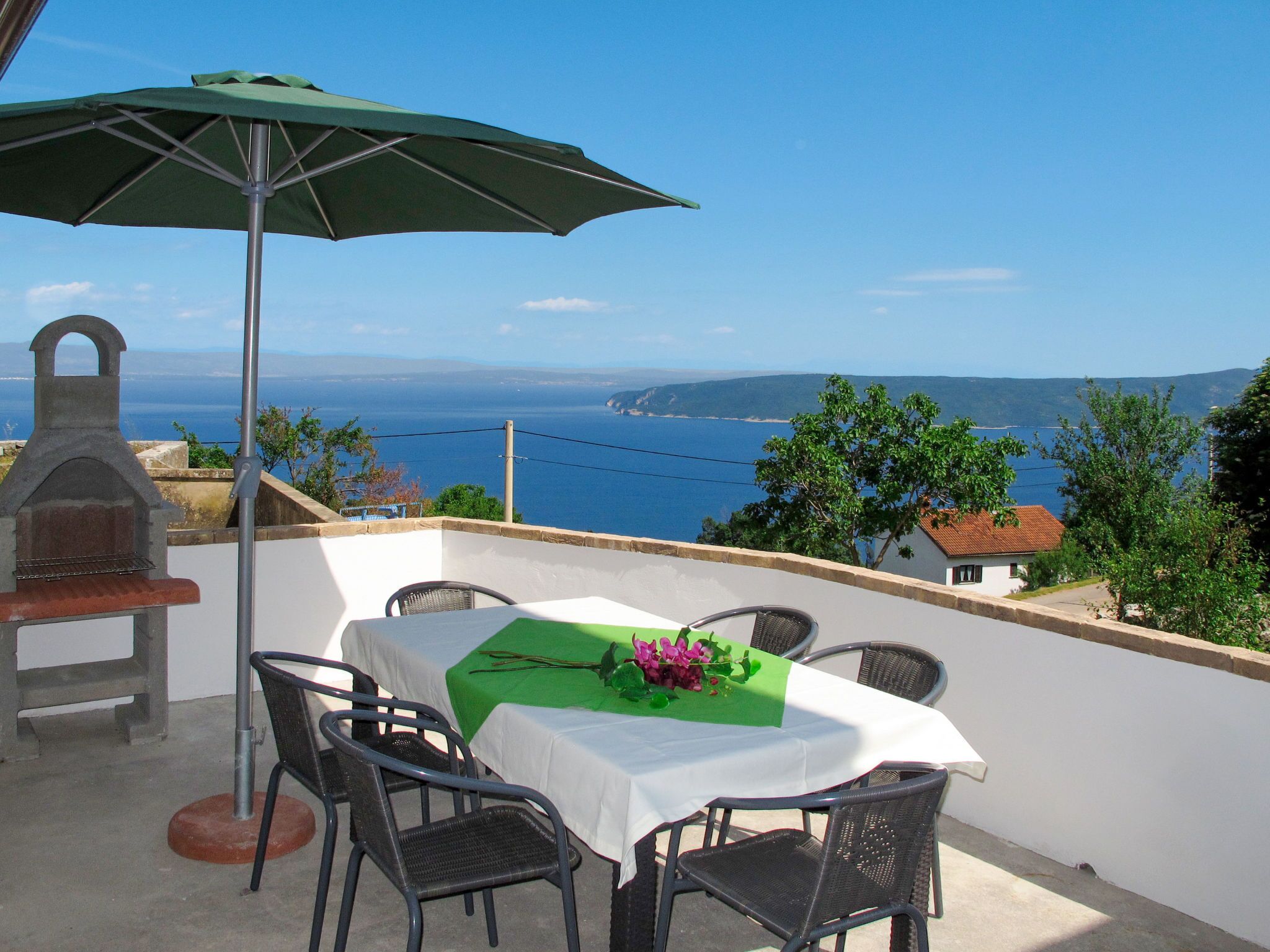 Eine Terrasse mit Tisch für zwei Personen, einem Grill und Meerblick.