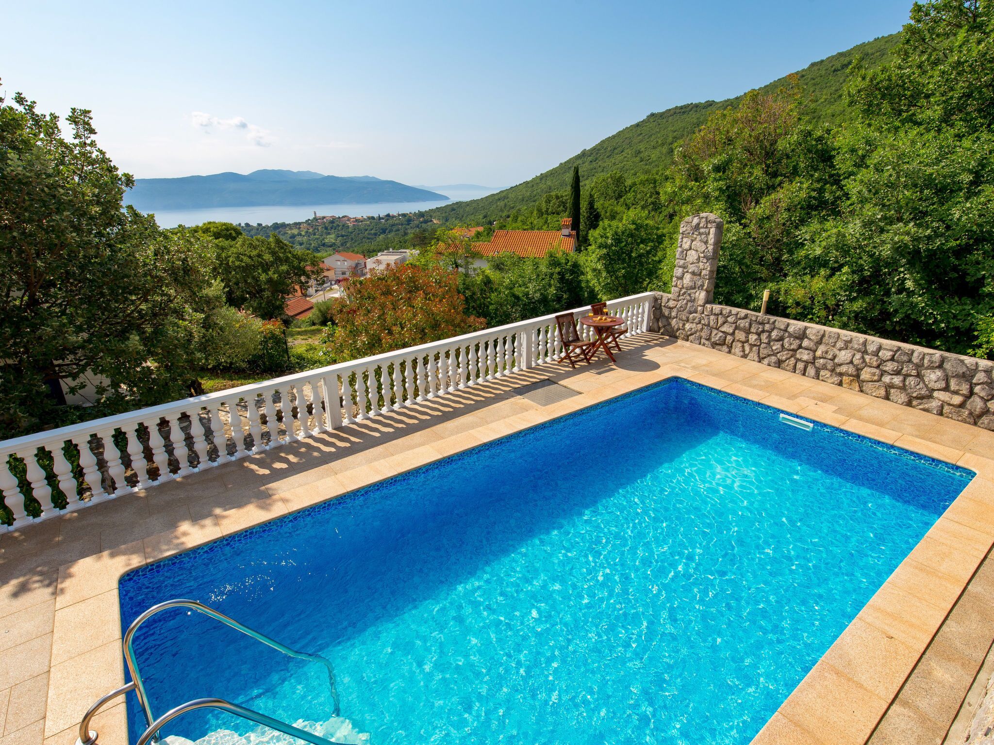 A rectangular swimming pool with a white balustrade, surrounded by a stone wall and a white fence.