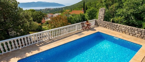 A rectangular swimming pool with a white balustrade, surrounded by a stone wall and a white fence.