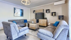 Een moderne woonkamer met grijze banken, een houten kast, een flatscreen televisie en een plafondlamp.