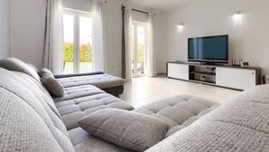 Een moderne woonkamer met een zithoek, een flatscreen televisie en een schuifpui naar een balkon.