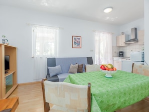 A compact living space with a sofa, a dining table with a green patterned tablecloth, a kitchen area with a microwave, and a coffee maker. - Apartment Nena by Interhome (Poreč)