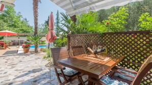 An outdoor patio with a wooden table and chairs, a pool, and lush greenery. - Apartment Nena by Interhome (Poreč)