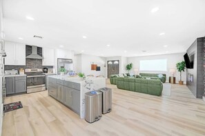 Una cocina moderna con armarios grises, una isla central, contenedores de basura de acero inoxidable y un área de comedor con un sofá verde.