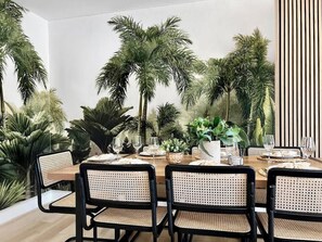 Un comedor con una mesa larga, sillas negras y diversas plantas.
