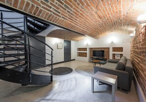 A modern living room with a brick ceiling, a spiral staircase, a grey sofa, a TV, and a fireplace.