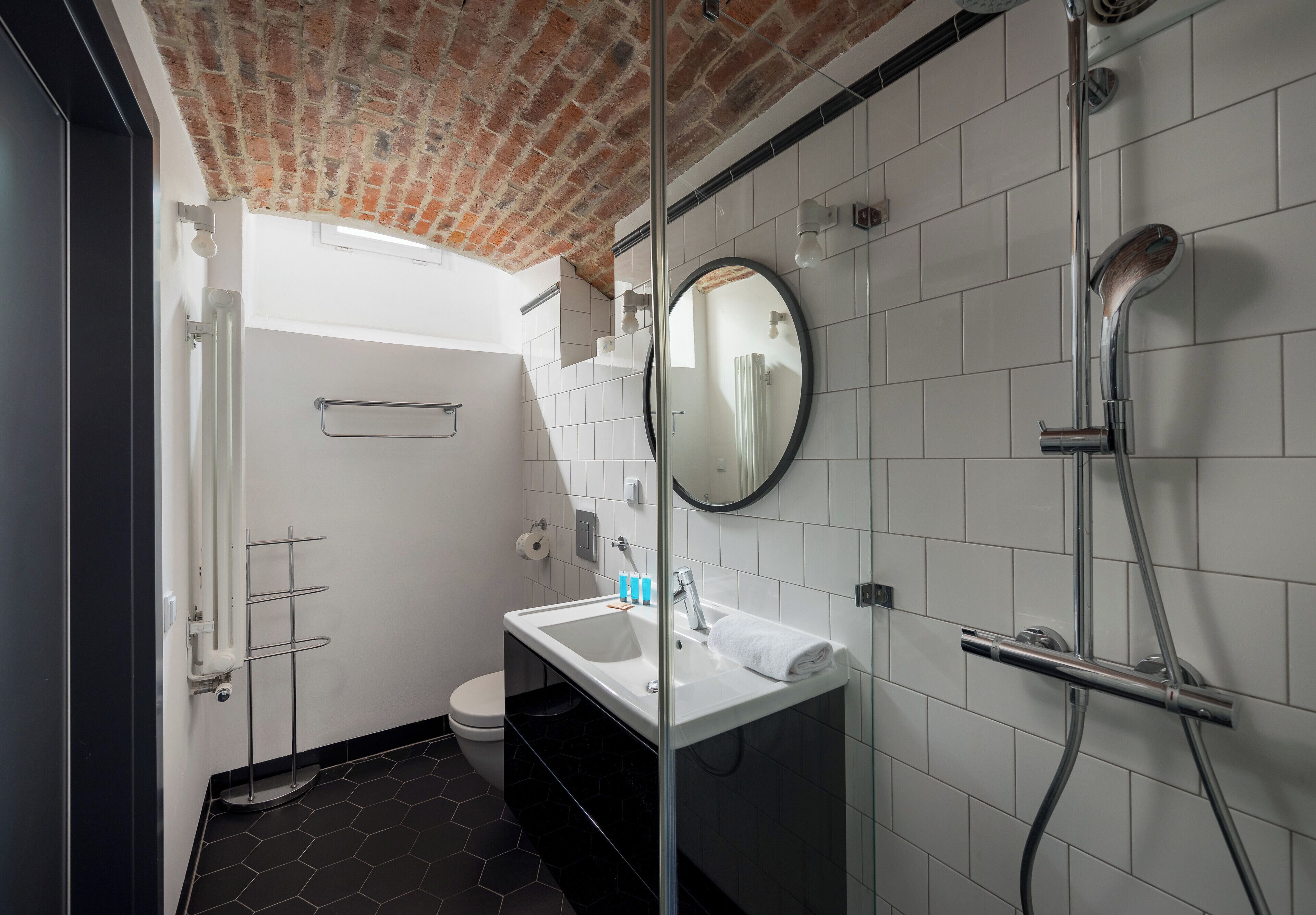 A modern bathroom with a white sink, a round mirror, and a shower.