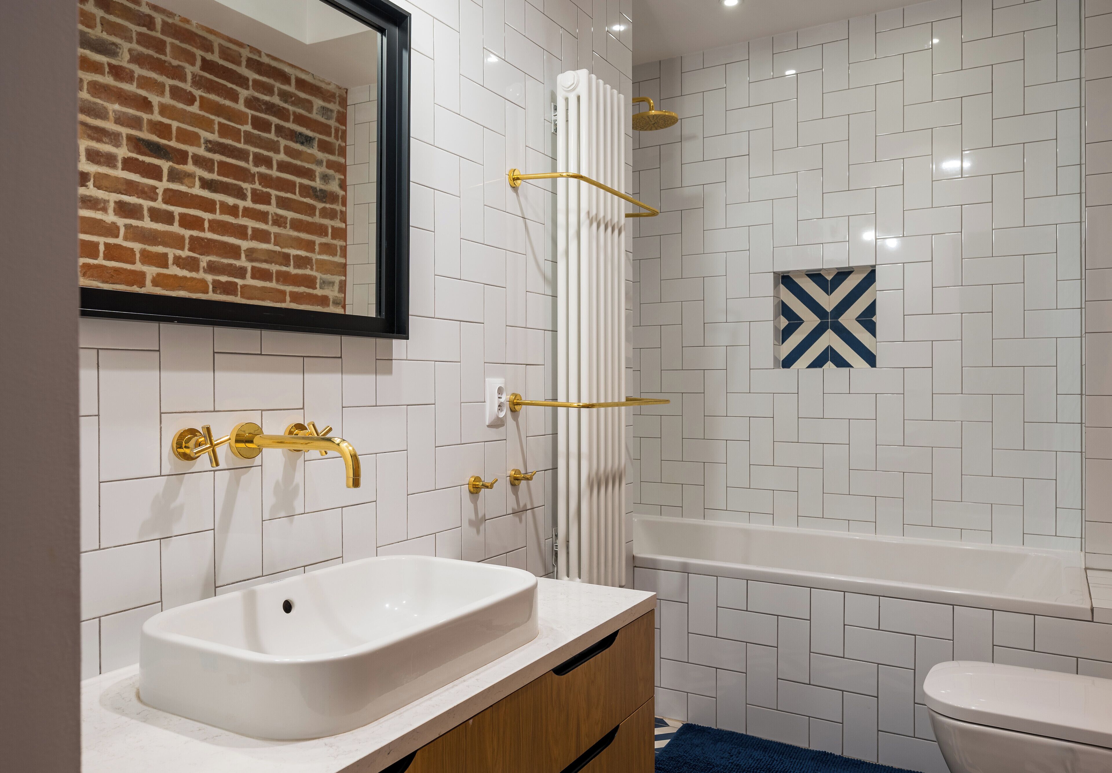 Une salle de bain avec un lavabo blanc, des robinetteries dorées, une douche avec un pommeau de douche doré et une baignoire blanche.