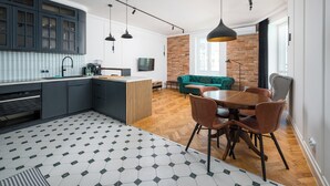 A modern kitchen with dark cabinets, a herringbone-patterned floor, and a dining area with a wooden table and chairs. - City Centre Stylish Apartment (Warszawa)