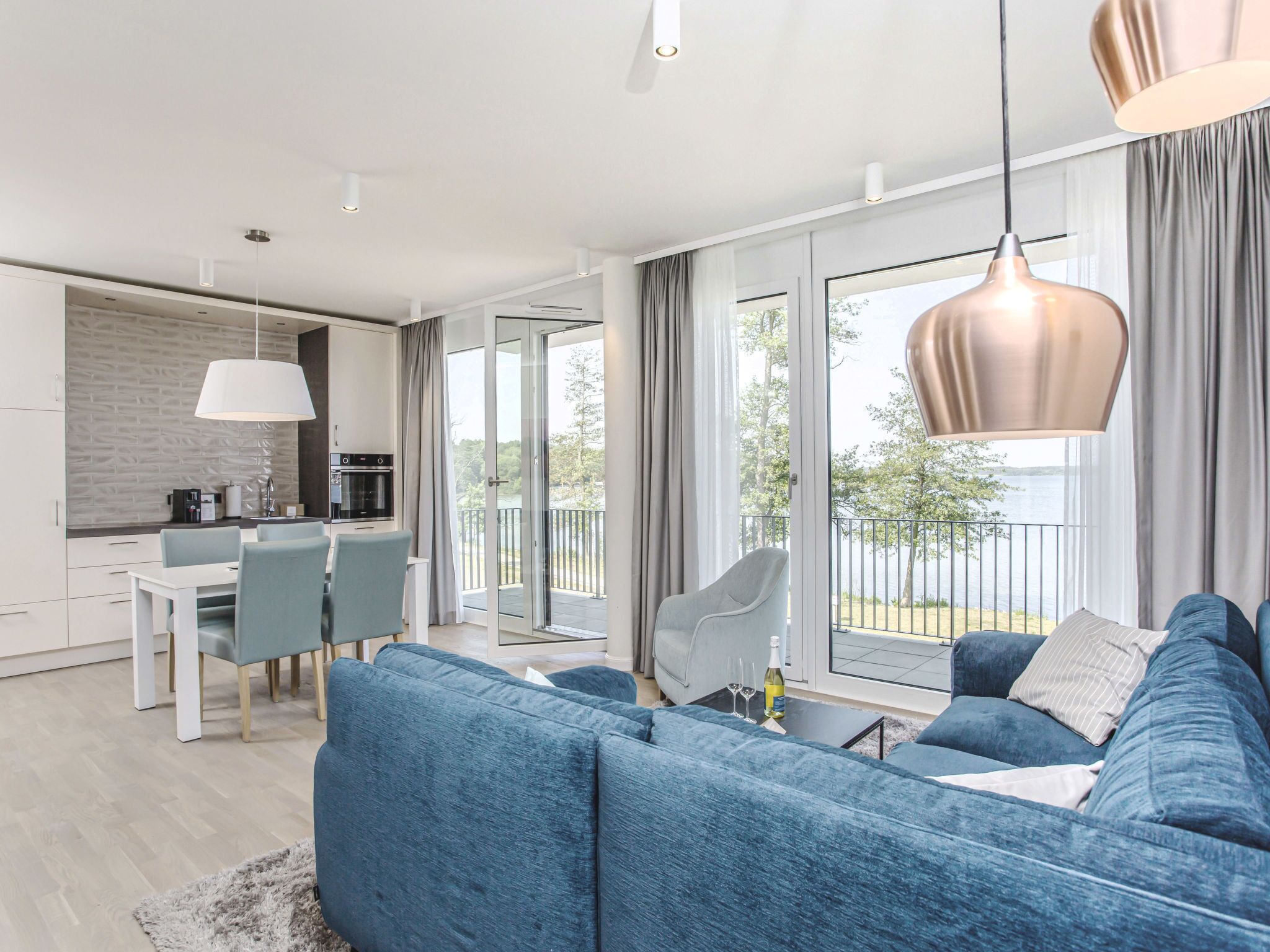 A modern living room with a blue sofa, a dining area, and a kitchen.