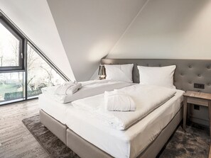 A modern bedroom with two beds, a large window, and a view of the outdoors.