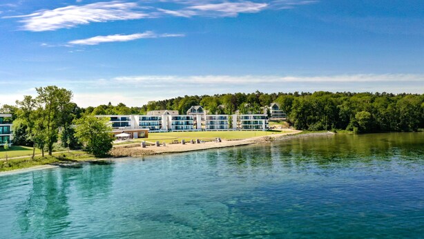 Ein am See gelegenes Hotel mit moderner Architektur, freiem Blick auf das Wasser und bewaldeter Umgebung.