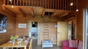 A cozy wooden cabin interior with a dining area, a living room with a red sofa, and a kitchen visible through an open door. - Alpenblick by Interhome (Illmensee)