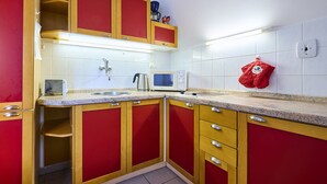 Een keuken met rode en houten kastjes, een magnetron, een waterkoker en een rode ovenhandschoen aan de muur.