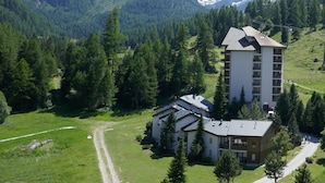 Eine Berglodge mit einem großen Hauptgebäude und einem Anbau, umgeben von dichtem Wald und schneebedeckten Bergen.
