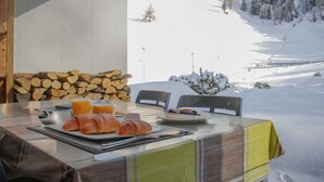 Ein Esstisch mit Croissants, Orangensaft und einer Schale Beeren, mit Blick auf eine verschneite Berglandschaft.