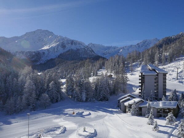 Une station de montagne enneigée, dotée d’une piste de ski, d’un immeuble imposant à plusieurs étages et d’une zone boisée.